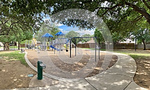 Drinking water fountain in public community park playground structure wood chips mulch, concrete sidewalk pathway, metal fence