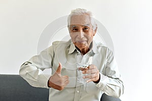 Drinking water is good healthy habit for old man, Elderly smiling asian man show thumb up to glass of purified water. photo