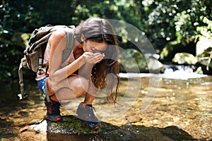 Drinking water, nature and woman by river in forest for thirst on adventure, trekking and explore outdoors. Travel