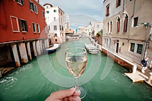 Drinking wine over Venice embankments. Bar visitor with glass of Prosseco walking past old houses of famous italian city