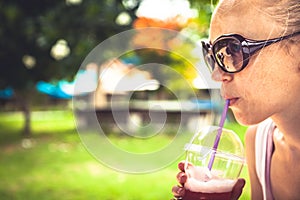 Drinking woman quenching her thirst with refreshing cold drink in hot summer day in park