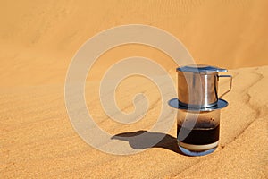 Drip Black Coffee in Vietnamese style with condensed milk on a red sand with copy space. Traditional method of making coffee.
