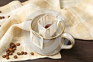 Drip coffee in cup and beans on brown wooden table, closeup