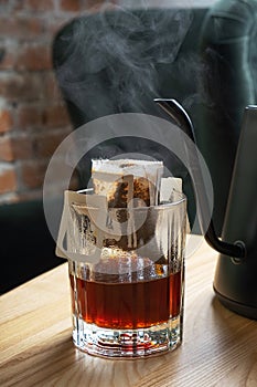 Drip coffee in a glass cup with a teapot on a wooden table in a beautiful interior