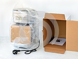 Drip-type coffee maker is in cellophane and near its cardboard box with instruction manual. Unpacking a new coffee machine.