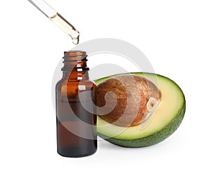 Dripping essential oil into bottle near cut avocado on white background
