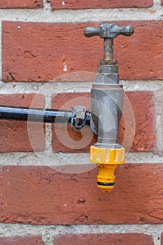 Dripping garden tap mounted on a brick wall