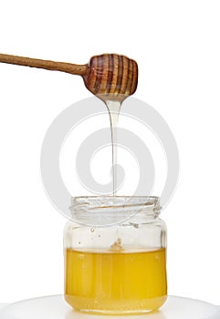 Dripping honey from honey dipper into jar of organic healthy sweet natural honey, isolated over white background with copy space