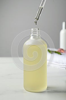 Dripping hydrophilic oil into bottle on white table, closeup