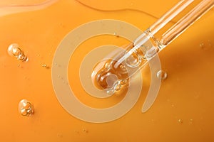Dripping hydrophilic oil from pipette on orange background, closeup