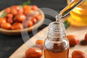 Dripping jojoba oil from pipette into bottle on blurred background