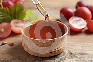 Dripping natural grape seed oil into bowl on table, closeup. Organic cosmetic