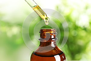 Dripping natural tea tree essential oil into bottle on blurred background