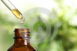 Dripping natural tea tree essential oil into bottle on blurred background, closeup