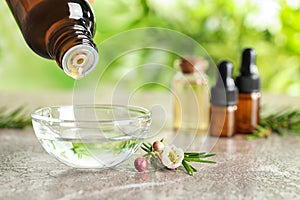 Dripping natural tea tree oil from bottle into bowl on table