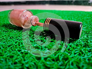 Dripping pink color nail polish bottle. Isolated on green background