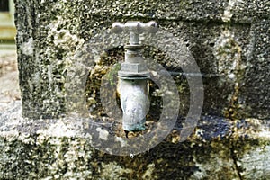 A dripping tap on an old water tank, a drip of water is caught in a spider\'s web