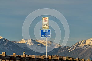Drive Alert and Buckle Up road sign against snowy mountain and cloudy sky