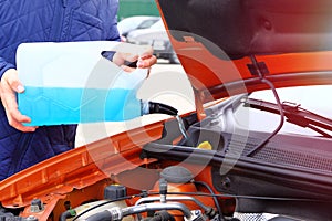 Driver with blue washer fluid in his hands, close up. Car maintenance concept. Filling windshield washer fluid on orange car