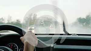 The driver drives the car in heavy rain, view through the windshield of the car