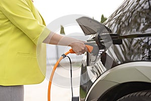 The driver of the electric car inserts the electrical connector to charge the batteries. Unrecognizable woman attaching