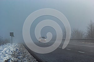 Driver of almost empty grey foggy misty rainy highway intercity road with low poor visibility on cold spring autumn morning.