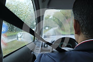 Driver with fastened seatbelt sitting in his car, seen from behind, on a rainy day