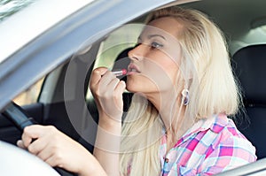 Driver a girl paints her lips at the wheel the car