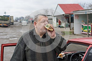 Driver gobbling lyulya kebab in lavash near his car