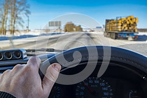 Driver hand behind the wheel of a car against the background of a winter landscape