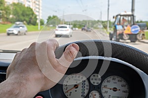 Driver hand on the steering wheel of a car that is overtaking a tractor