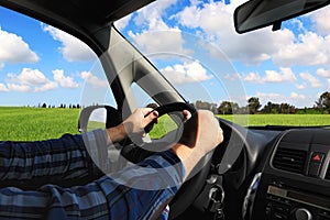 Driver hands on car steering wheel. Dashboard. Green field countryside. Windshield and side window view. Driving car on nature