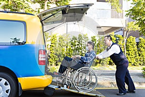 Driver helping man on wheelchair getting into taxi