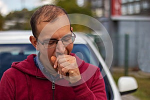 The driver with his eyes closed yawns in front of the car.