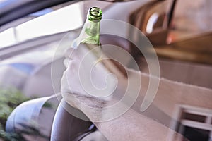 Driver holding a beer bottle and the steering wheel - drinking and driving concept