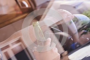 Driver holding a beer bottle and the steering wheel - drinking and driving concept