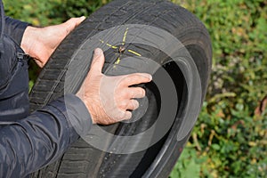 Driver holding in hands damage car tire with nail and yellow mark. Flat car tire