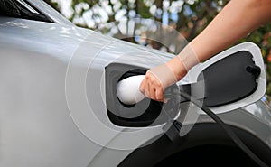 The driver inserts the electrical connector to charge the batteries. Hand holding plug in cable while charging electric car..