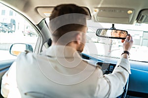 Driver looks in the rearview mirror. Man adjusts the mirror in the car.