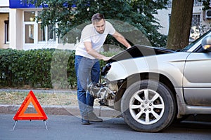 Driver man looking on wrecked car in car accident. Man regrets about fixing car after auto crash. Tragedy car collision. Dangerous