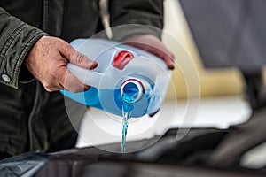 Driver refilling the blue non-freezing windshield washer liquid in the tank of the car, close-up