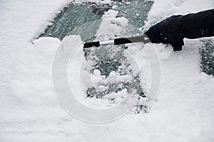 Driver is removing snow from car windshield with ice scraper and broom, clean car window from icy frost, winter season