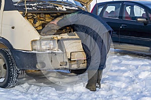 The driver repairs the engine of the car in the winter in the cold