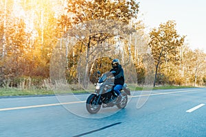 Driver riding motorcycle on empty road in beautiful autumn forest.