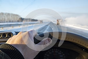 The driver`s hand on the steering wheel of the car that is catching up with the truck