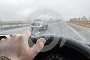 Driver`s hand on the steering wheel of a car that is driving on the highway