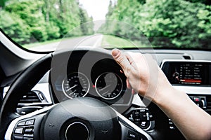 Driver`s hand on steering wheel on forest background. Driving car concept.