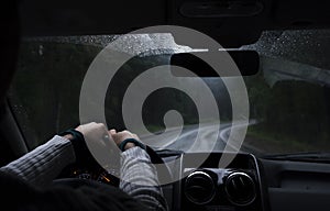 Driver`s hand on a steering wheel inside a car on a road