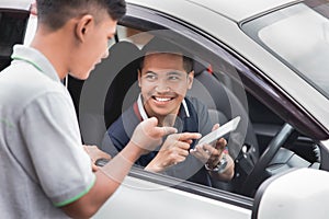 Driver showing his mobile phone to a man standing next to his ca