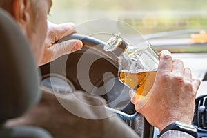 The driver is sitting behind the wheel and holding a bottle of alcoholic drink. Breaking the law and drinking alcohol while